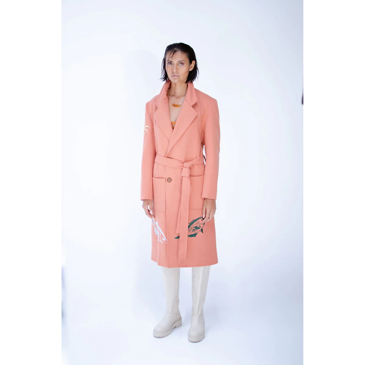 A fashion model wearing and styling a minimalist outfit with white boots and a pink trench coat in a contemporary style by OnPost 